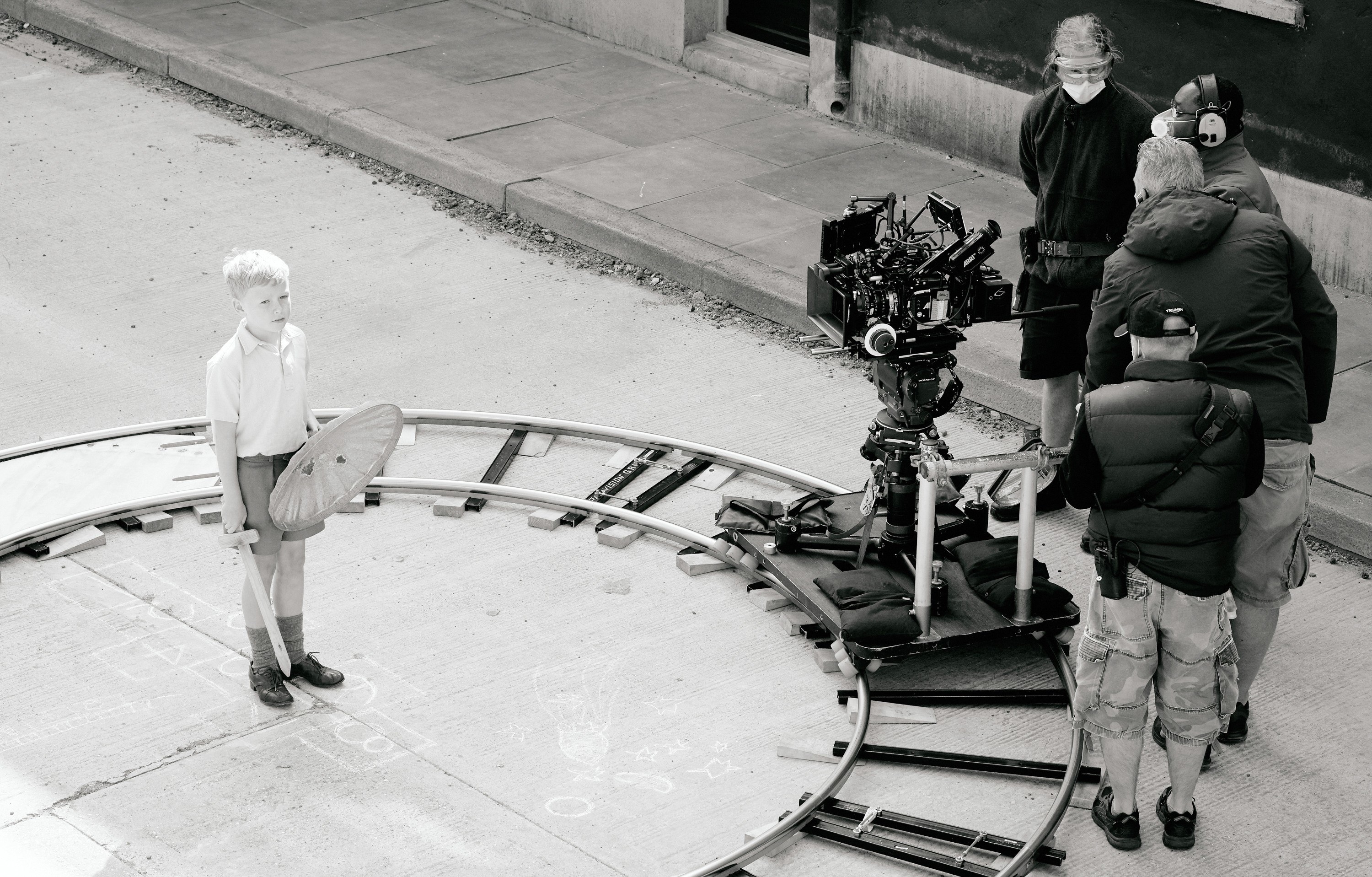 A camera crew set up circling around the young actor Jude Hill, who holds a toy sword and garbage can lid shield