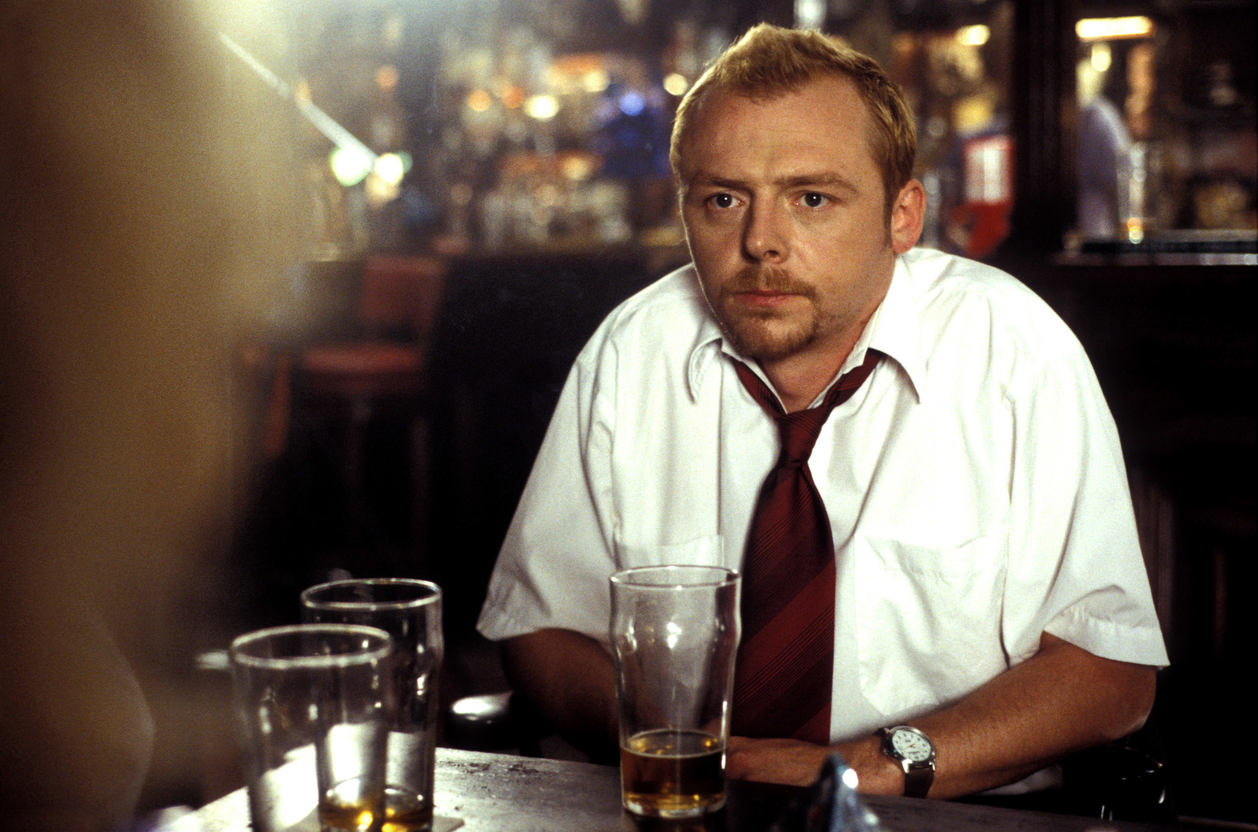 Simon Pegg in a shirt and tie, sitting dejected in a pub with a nearly empty pint of beer
