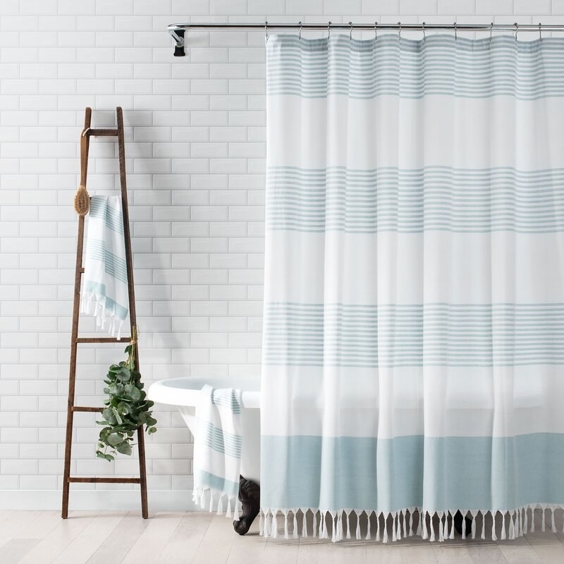 a stripped shower curtain with bottom tassels slightly covers a claw-foot bath tub