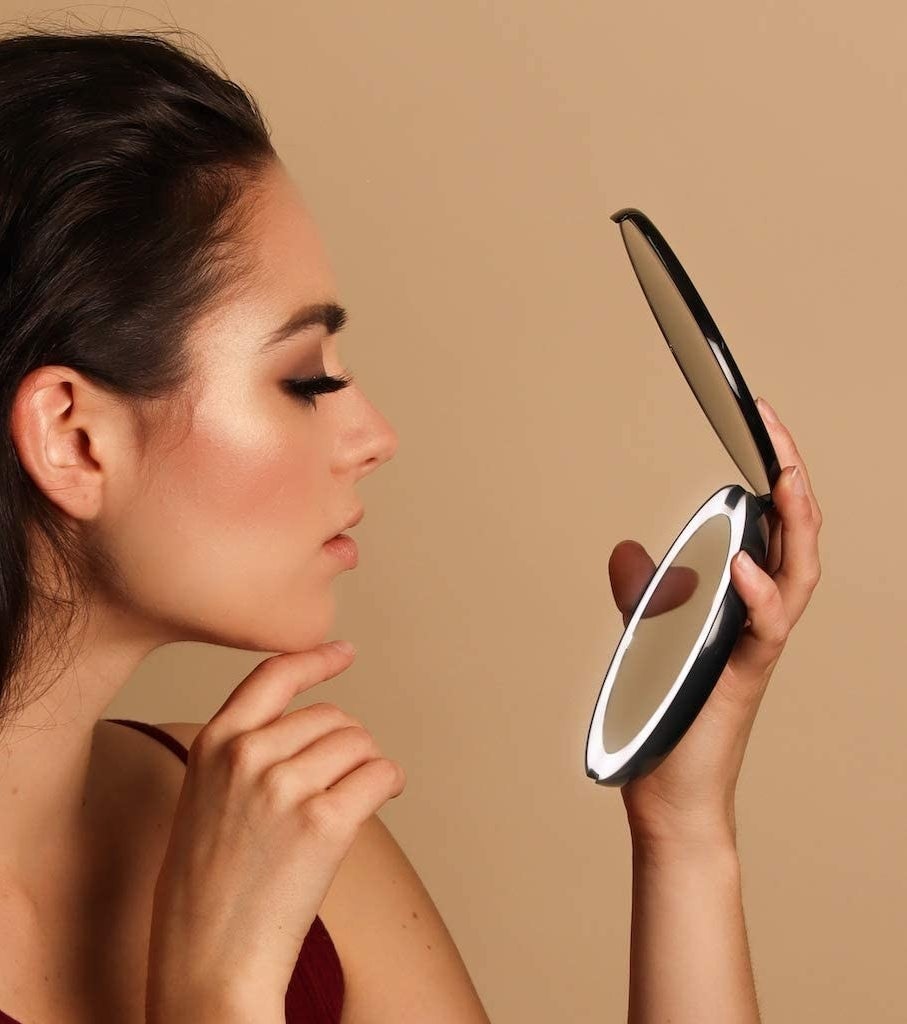 A person using the compact mirror against a plain background