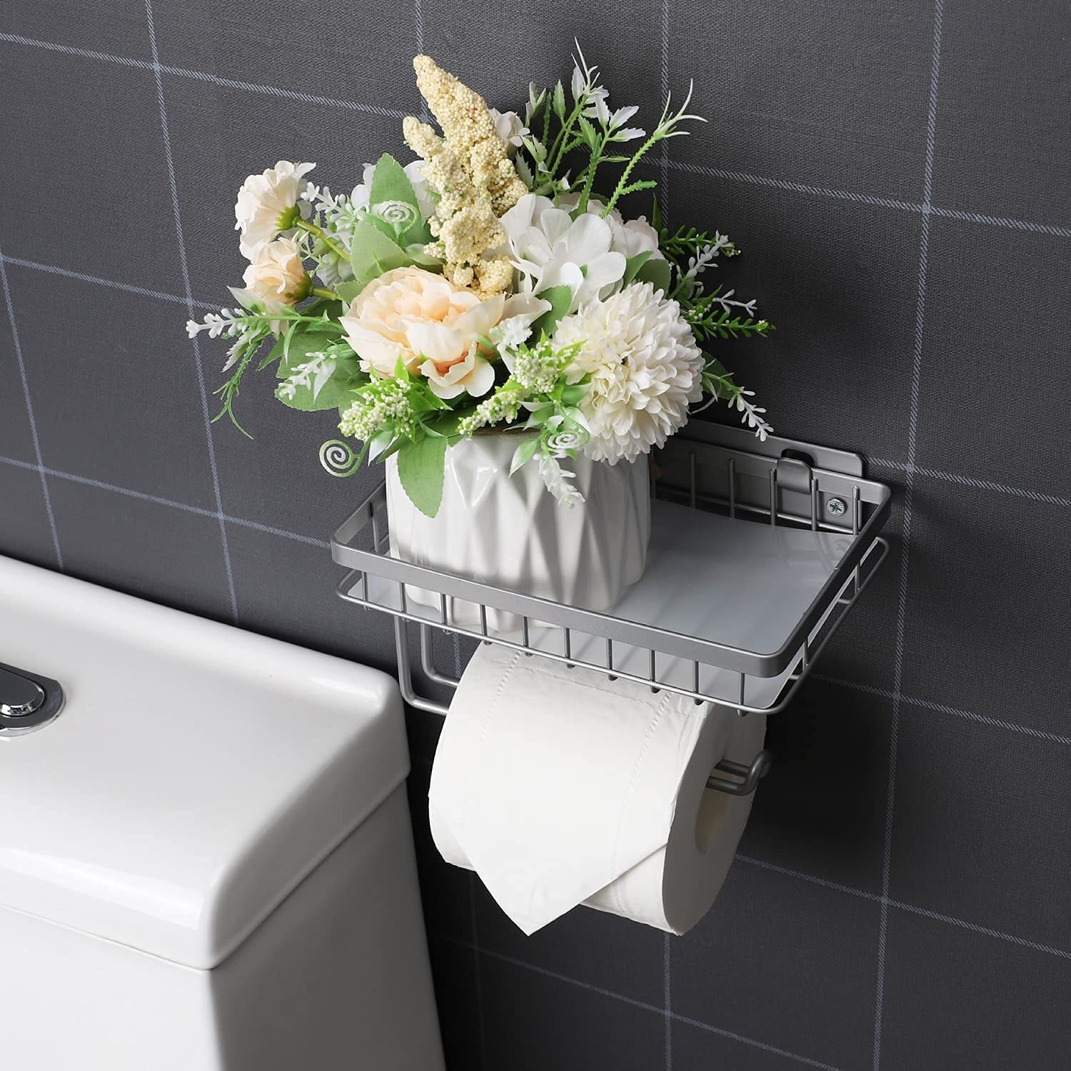 The toilet paper holder in a bathroom with some flowers on top of it