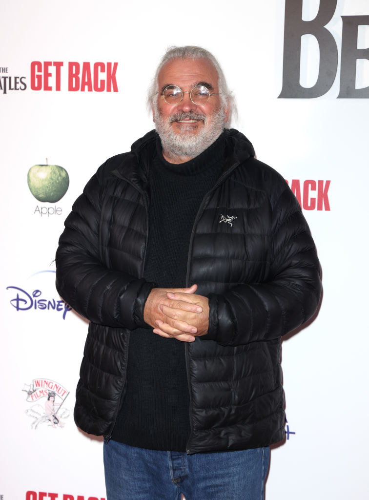 wearing round glasses and a puffer jacket, the director smiles on the red carpet