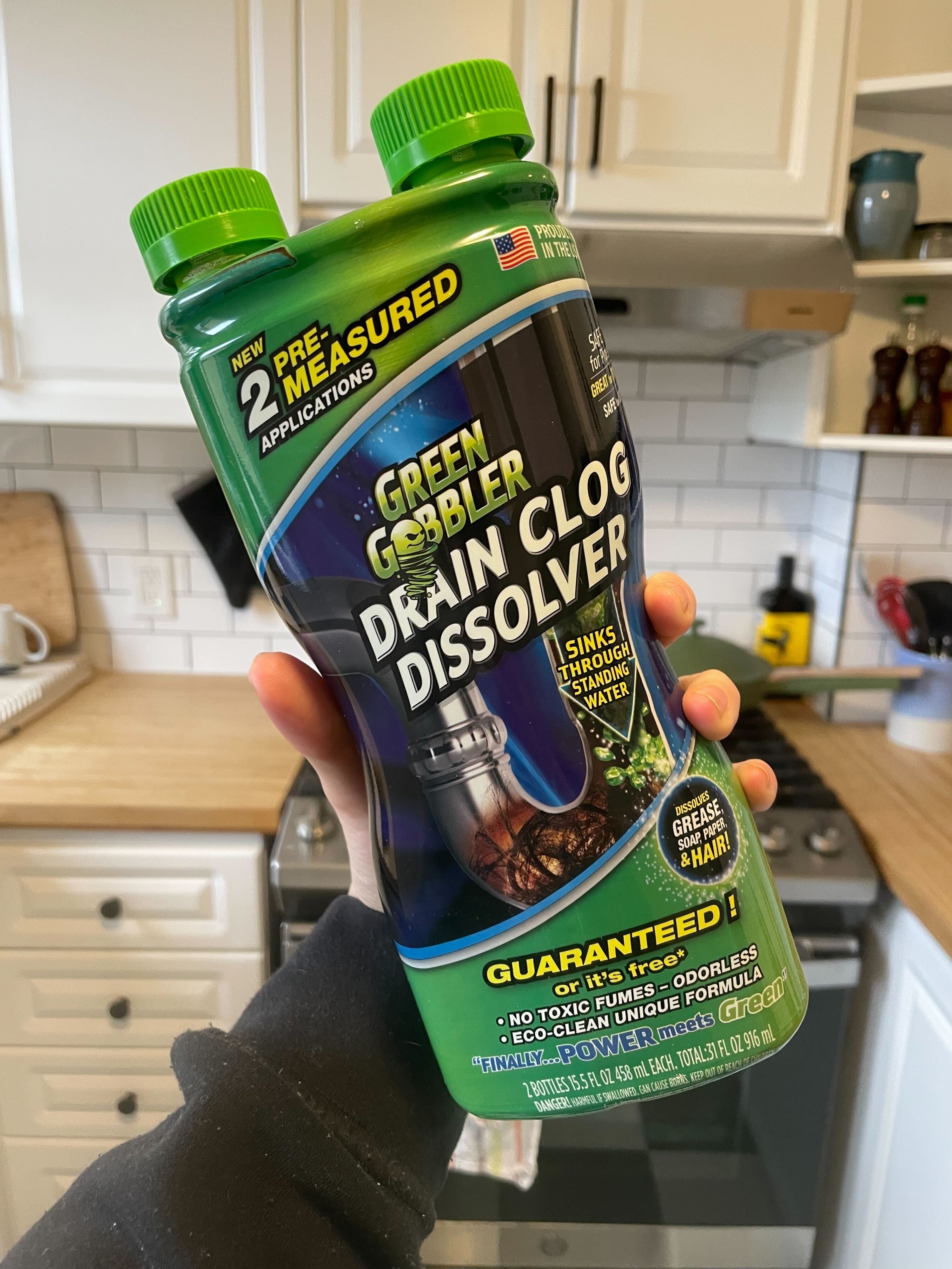a person holding up a bottle of the green gobbler drain cleaner