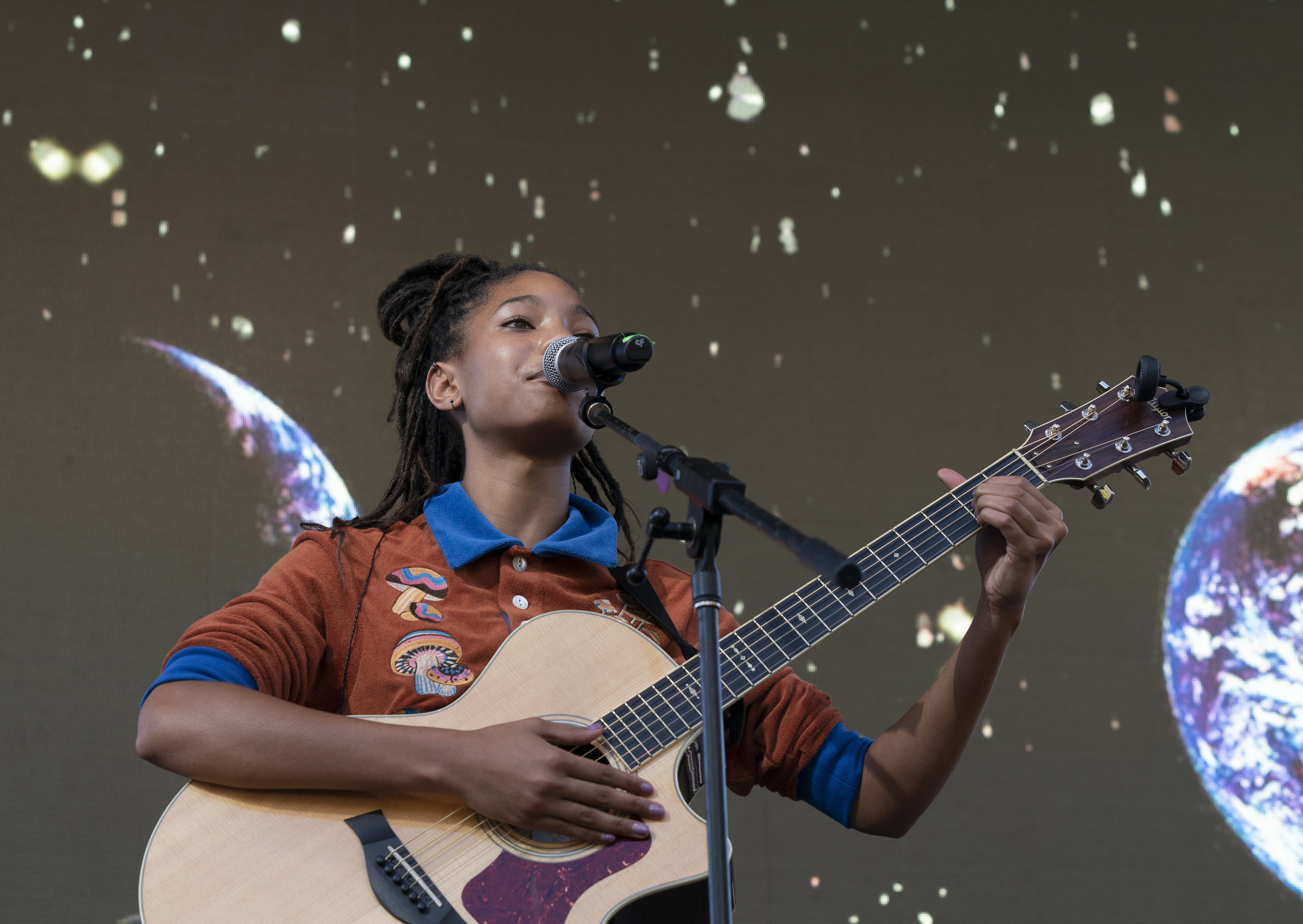 Willow singing onstage with a guitar and a view of space as a backdrop