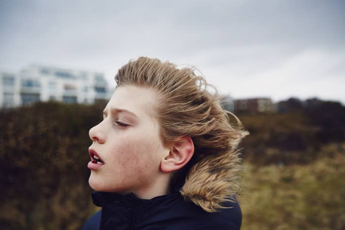 A boy, eyes closed, stands in the wind on a gray day