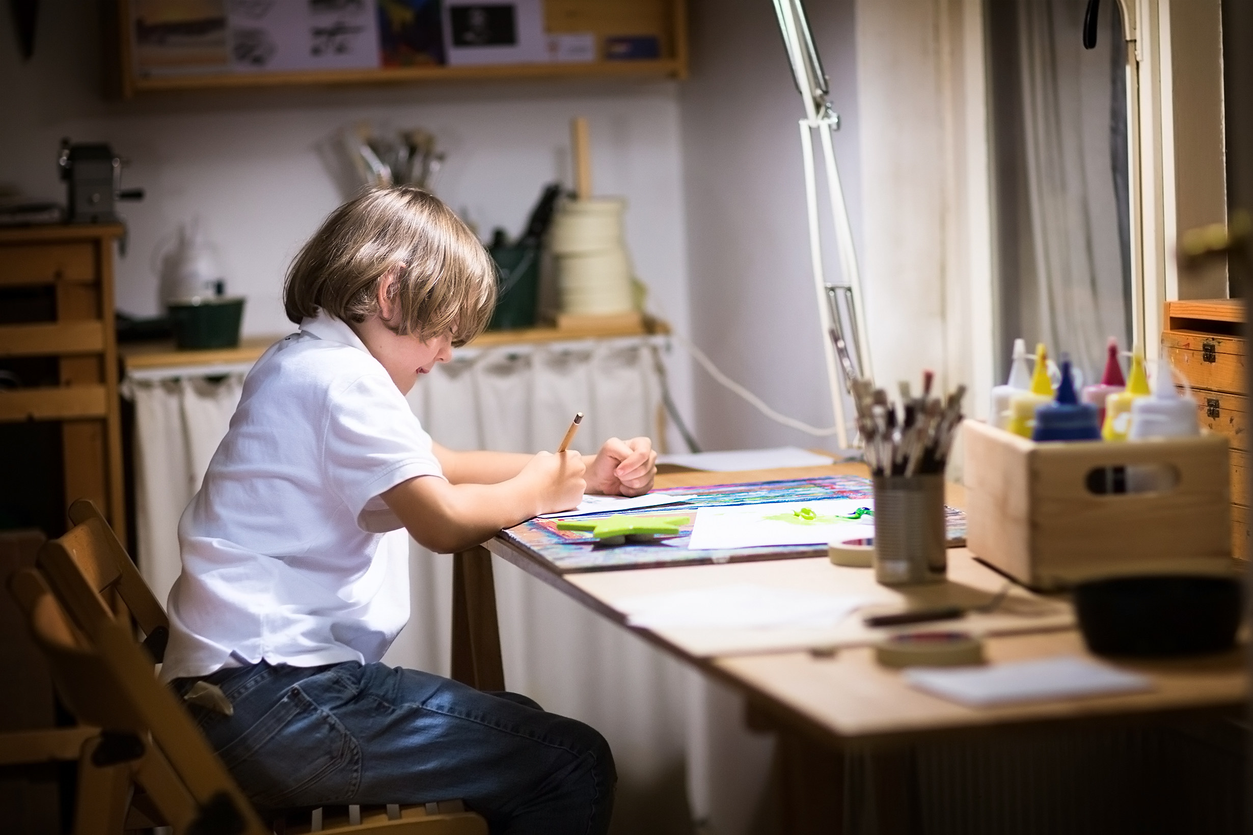 A boy in his room at night, drawing at at his desk