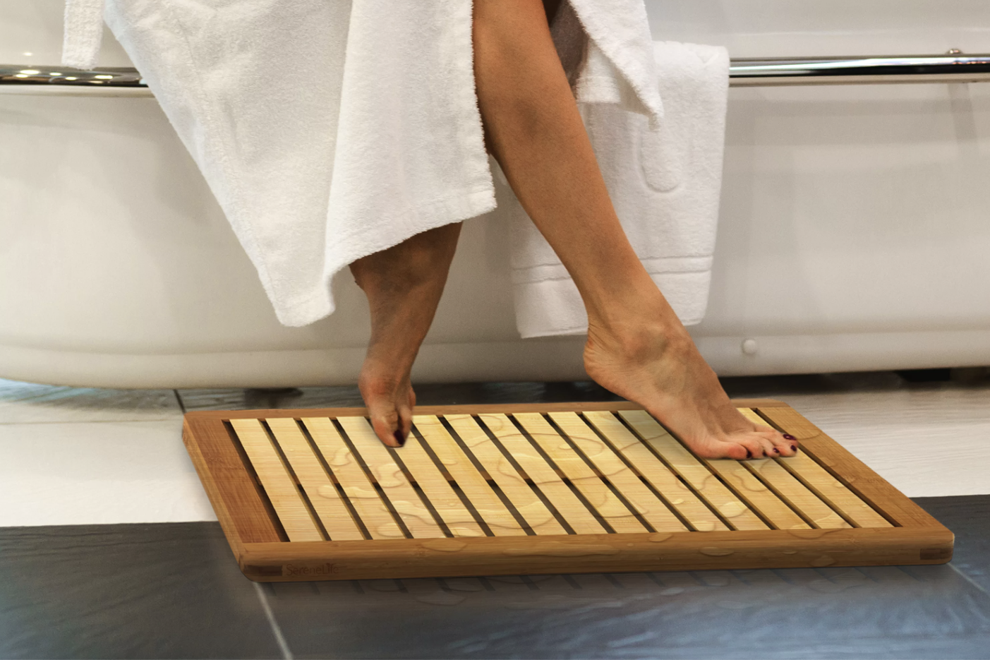 the teak bath mat with a person&#x27;s feet on it