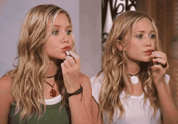 Mary Kate and Ashley Olsen putting on lipstick