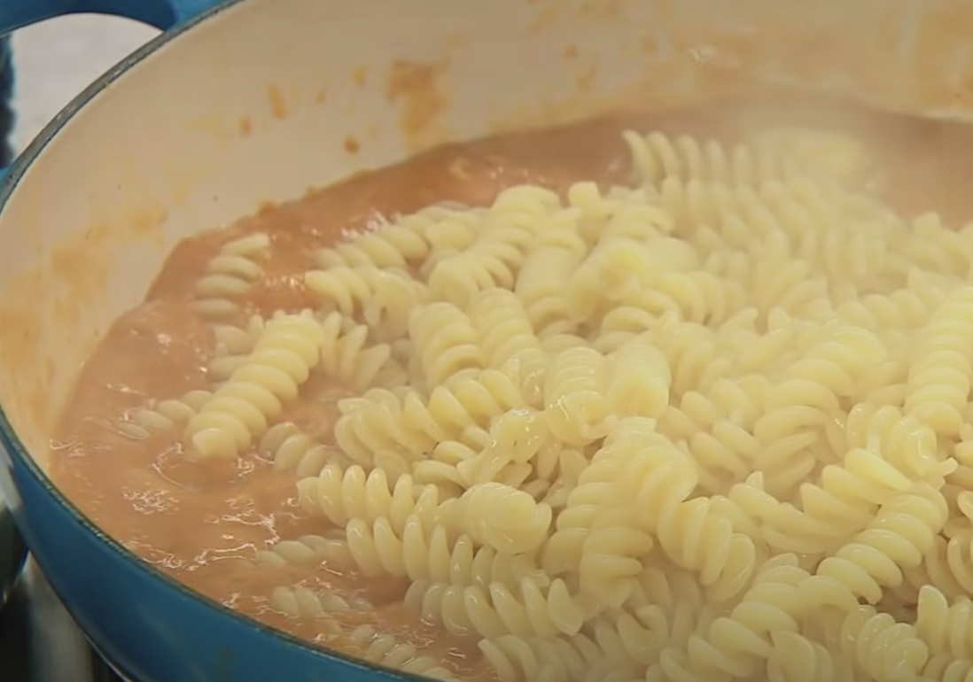Pumpkin puree mixed with rotini pasta in a cooking vessel