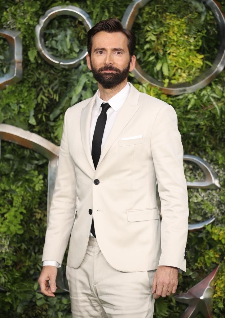 David wears a light suit in front of a foliage background