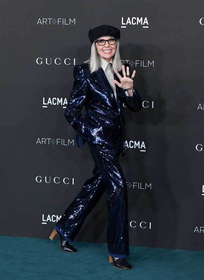 Diana Keaton walks a step and repeat in a sparkly suit, boots, and a beret