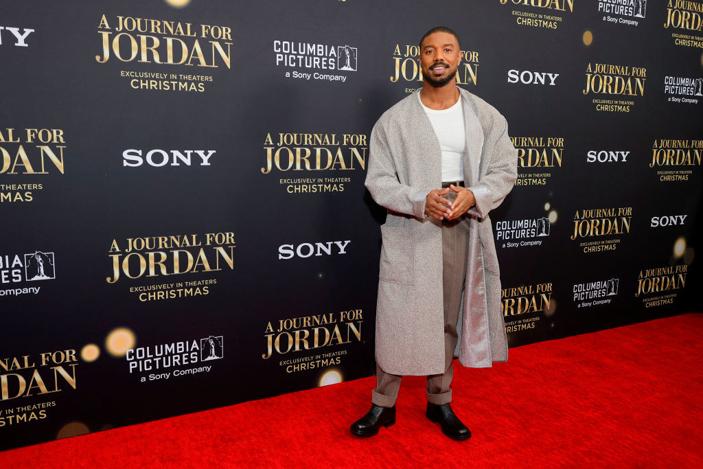 Michael wears a long coat over slacks and a T-shirt for a red carpet event
