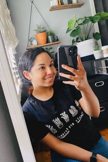 a reviewer posing for a mirror selfie while wearing the black t-shirt