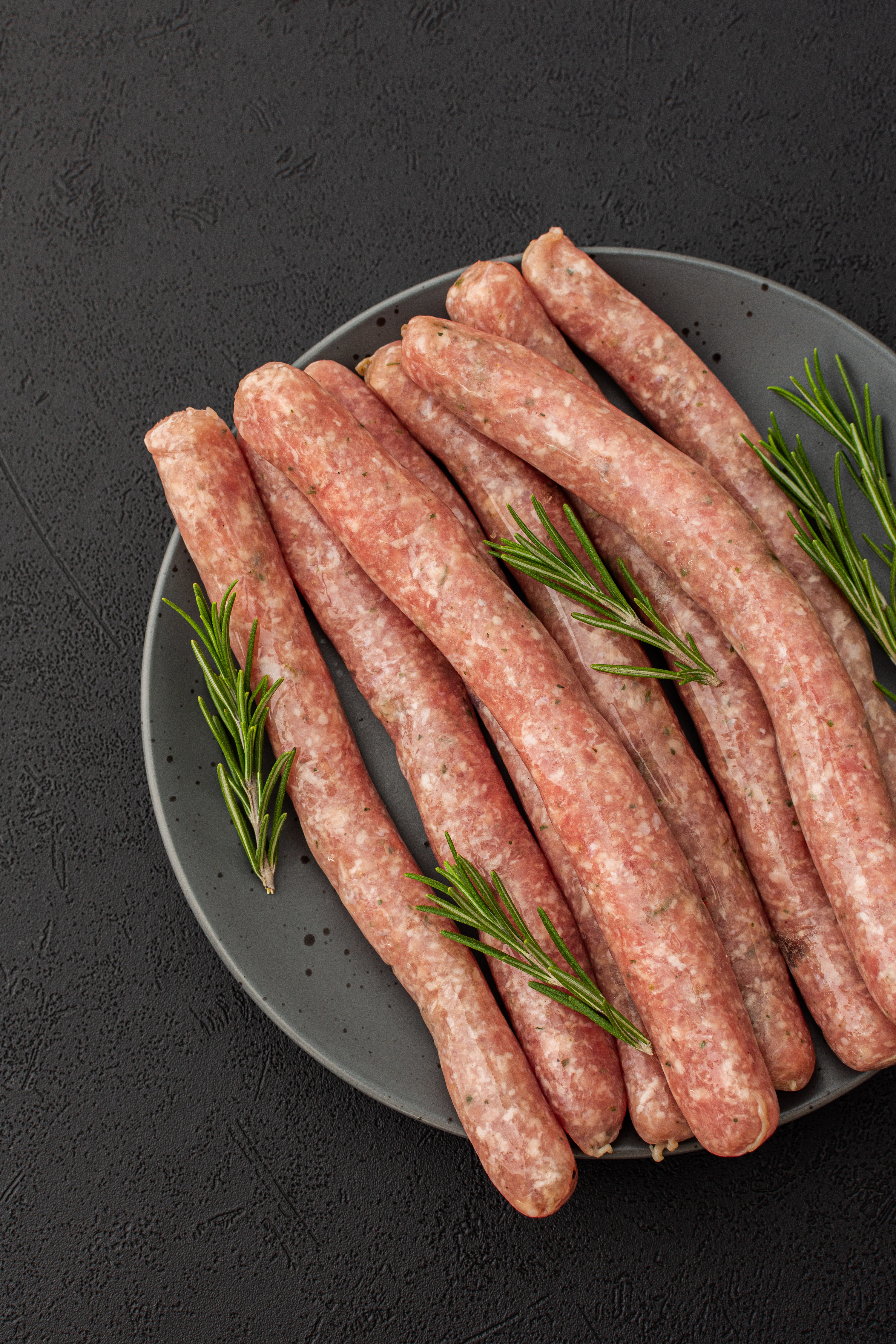A plate of raw sausage with sprigs of rosemary garnish