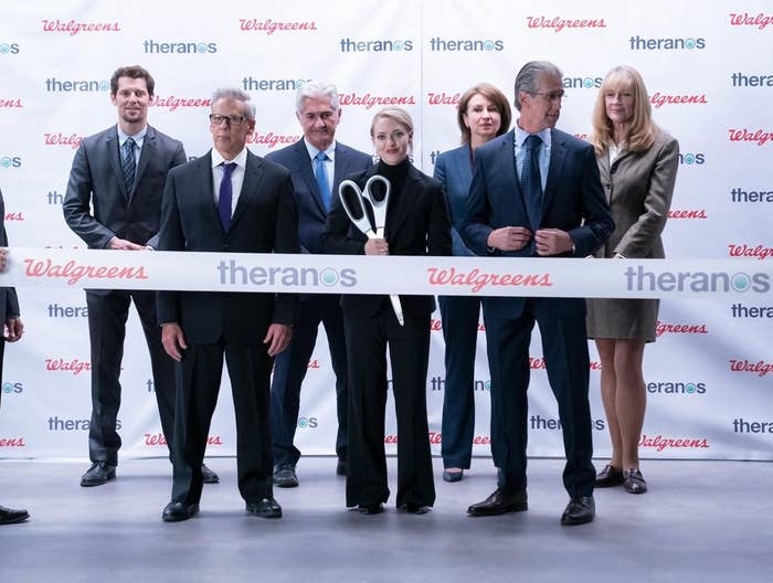 A group of people stand in front of a large banner that says &quot;Theranos&quot; in the show