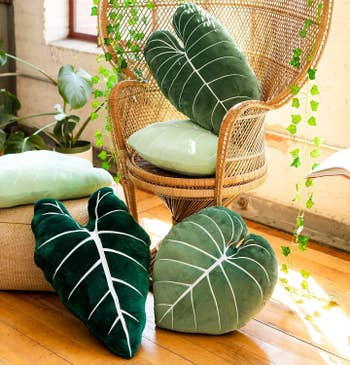 a collection of the plant pillows sitting on and around a wicker chair
