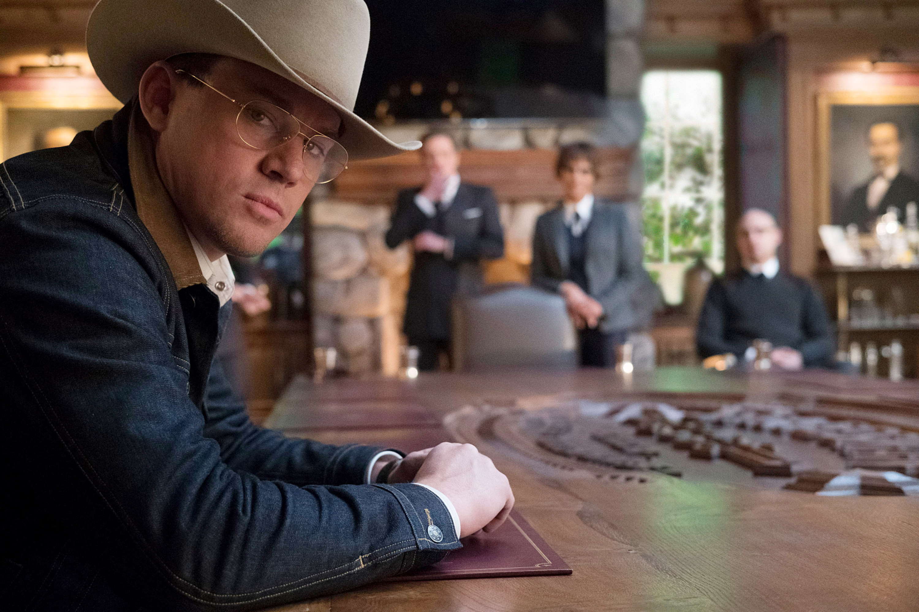 Tatum wearing a cowboy hat and sitting at a board room desk with three people looking at him