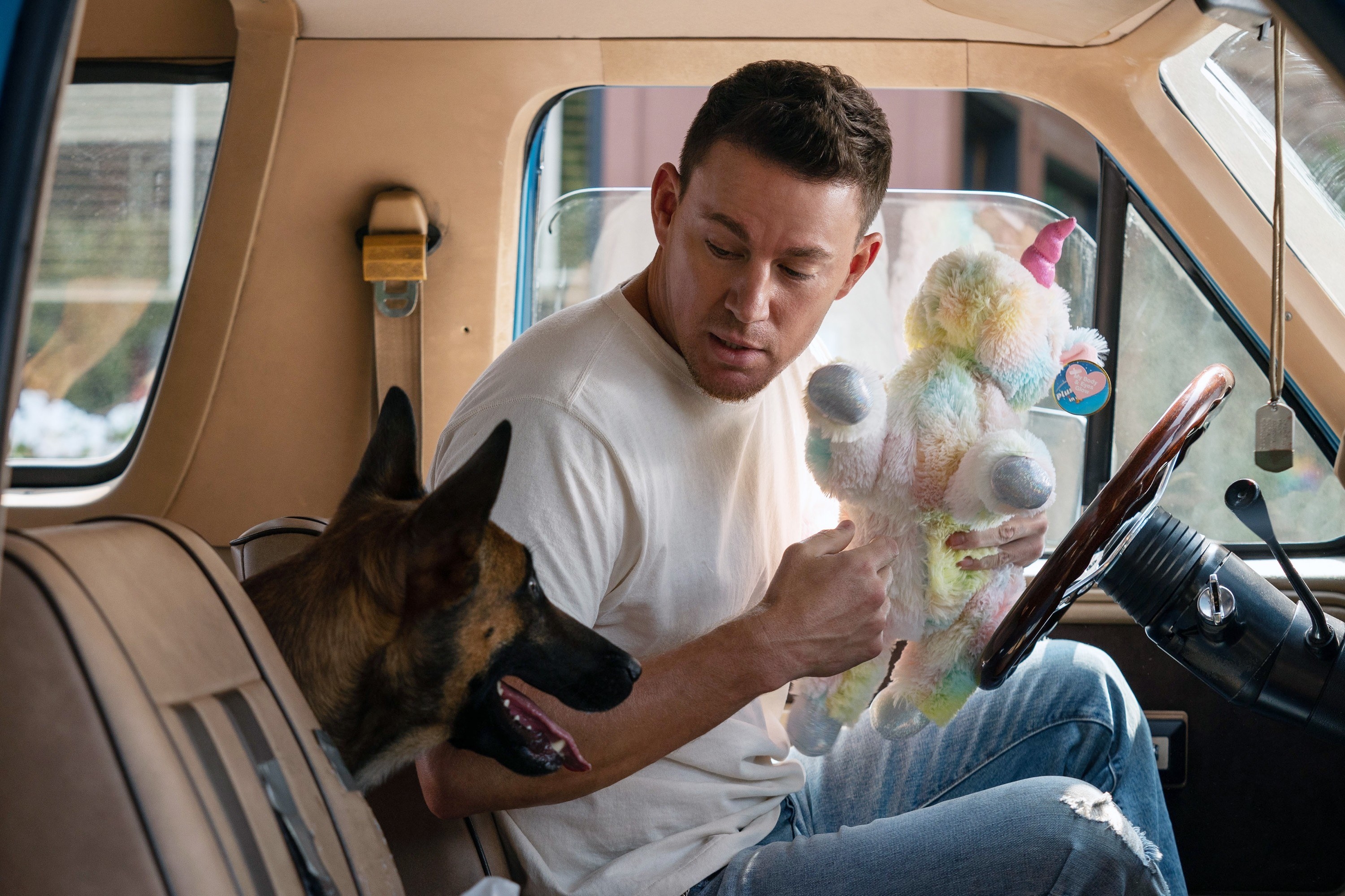 Tatum in a car with his dog and holding a unicorn toy for her
