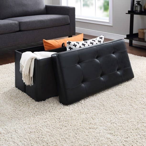An image of a collapsible storage ottoman with a removable lid and durable faux black leather upholstery