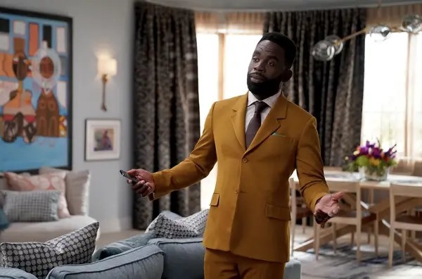 Jimmy Akingbola as Geoffrey Thompson in &quot;Bel-Air&quot; wears a smart suit and stands in a clean living with his arms outstretched in a welcoming manner