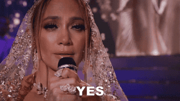 JLo wears a jeweled head veil with a mic in her hand saying, &quot;yes&quot;