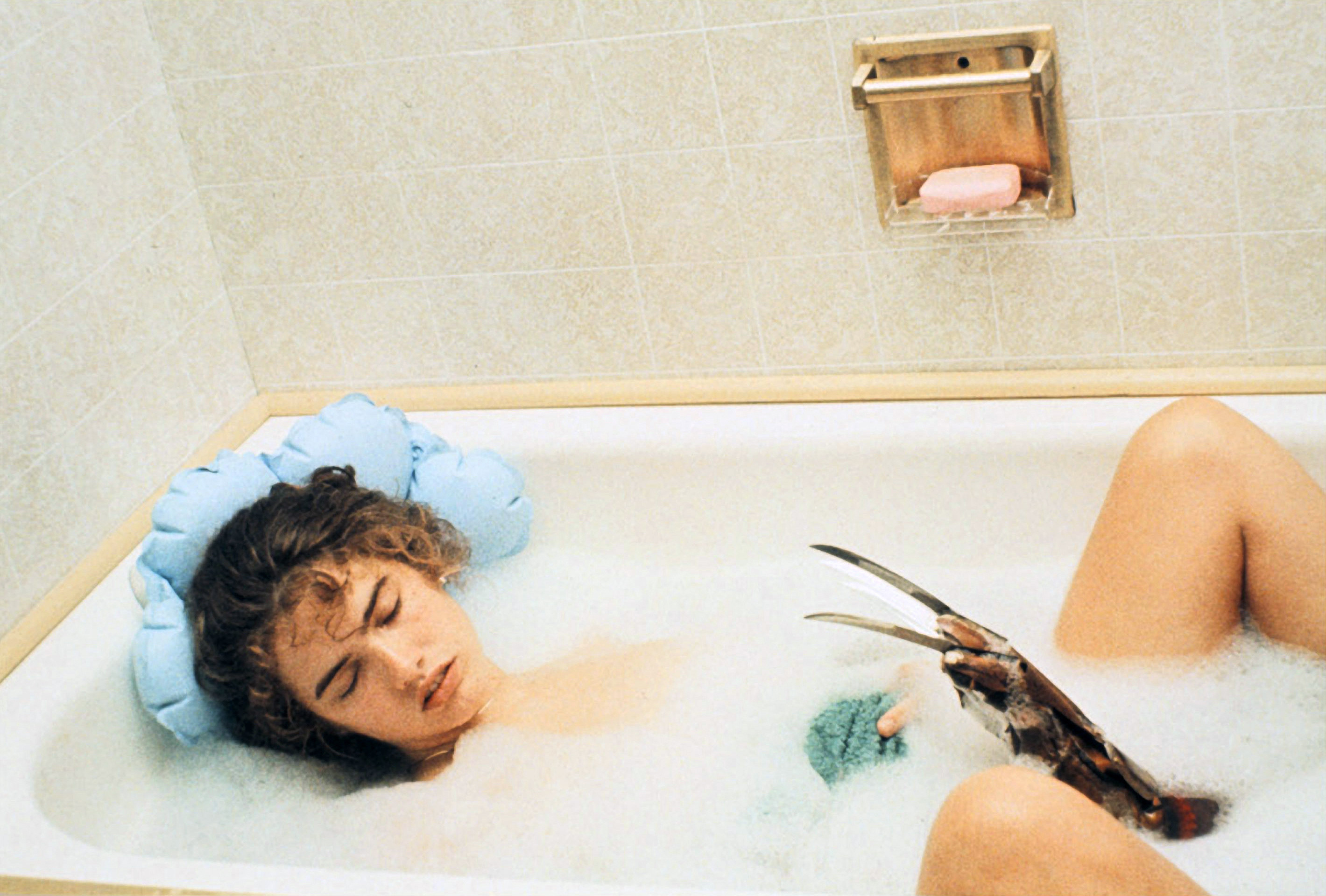 Heather Langenkamp asleep in a bubble bath with Freddy Krueger&#x27;s claw coming up from the water
