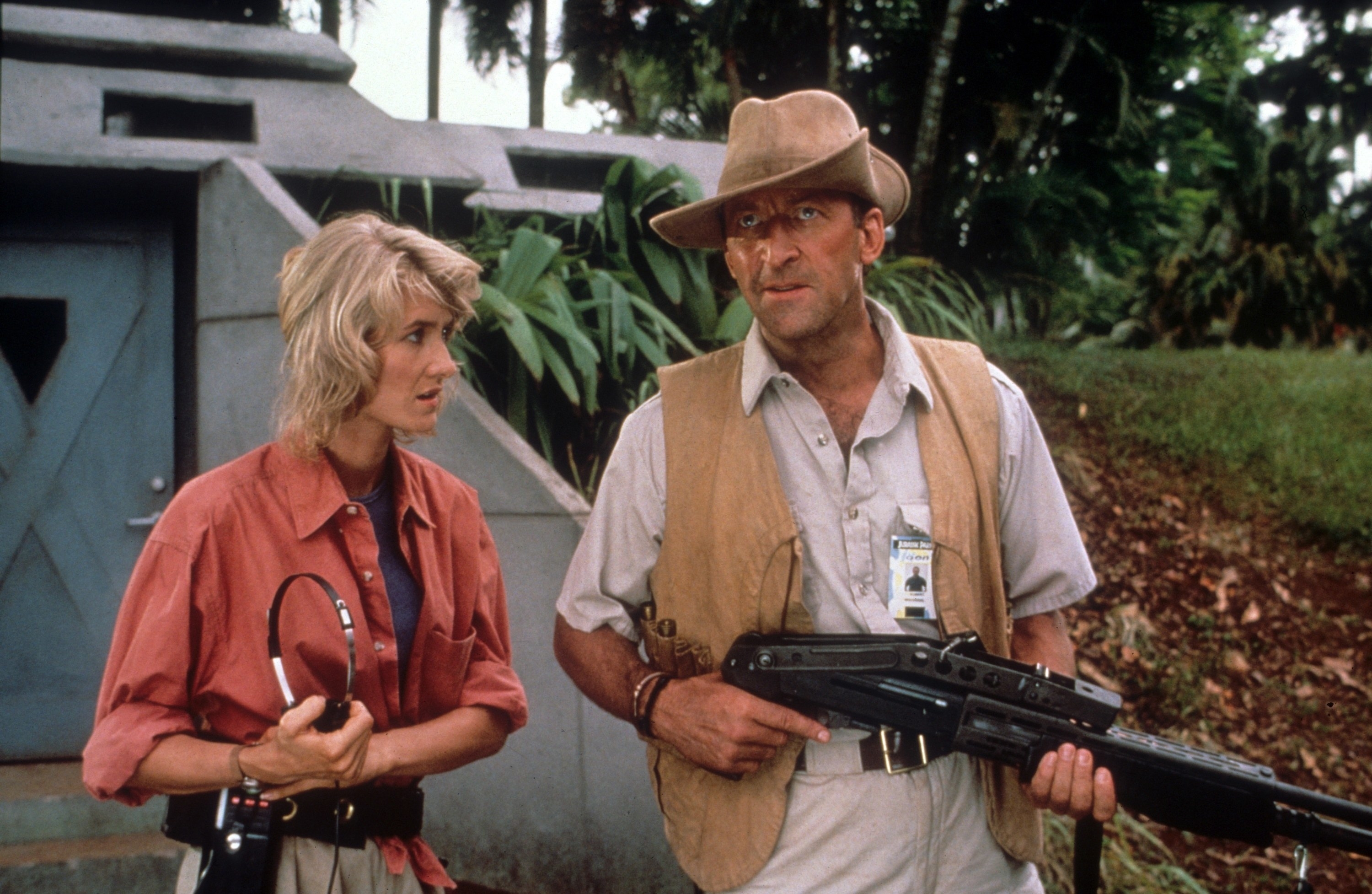 laura dern standing next to bob peck who is holding a gun in a forest in jurassic park
