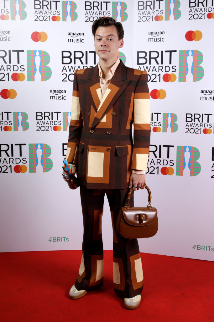 Harry wears a color-block suit with flared pants and carries a purse on the red carpet