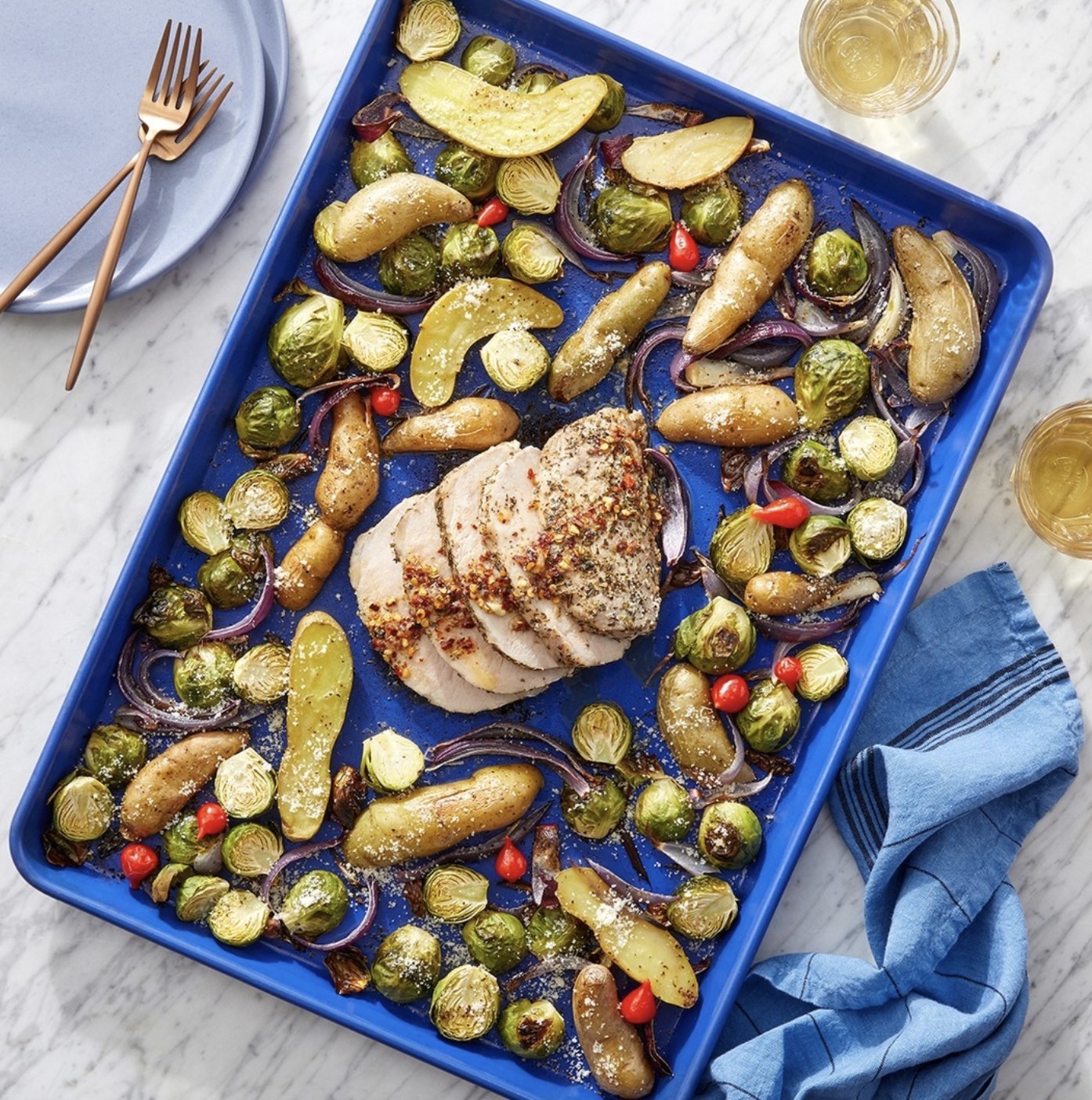 A sheet pan of roasted veggies and potatoes with chicken in center