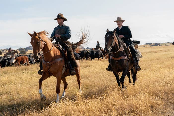 Two men wearing wide-brimmed hats ride on horses