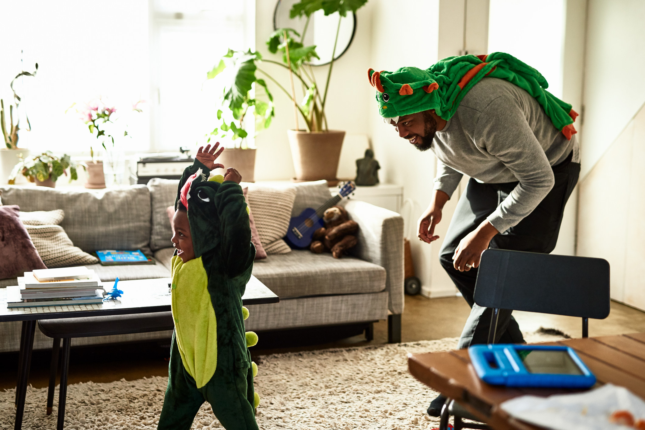 A parent in a dinosaur costume chases a child in a dinosaur onesie