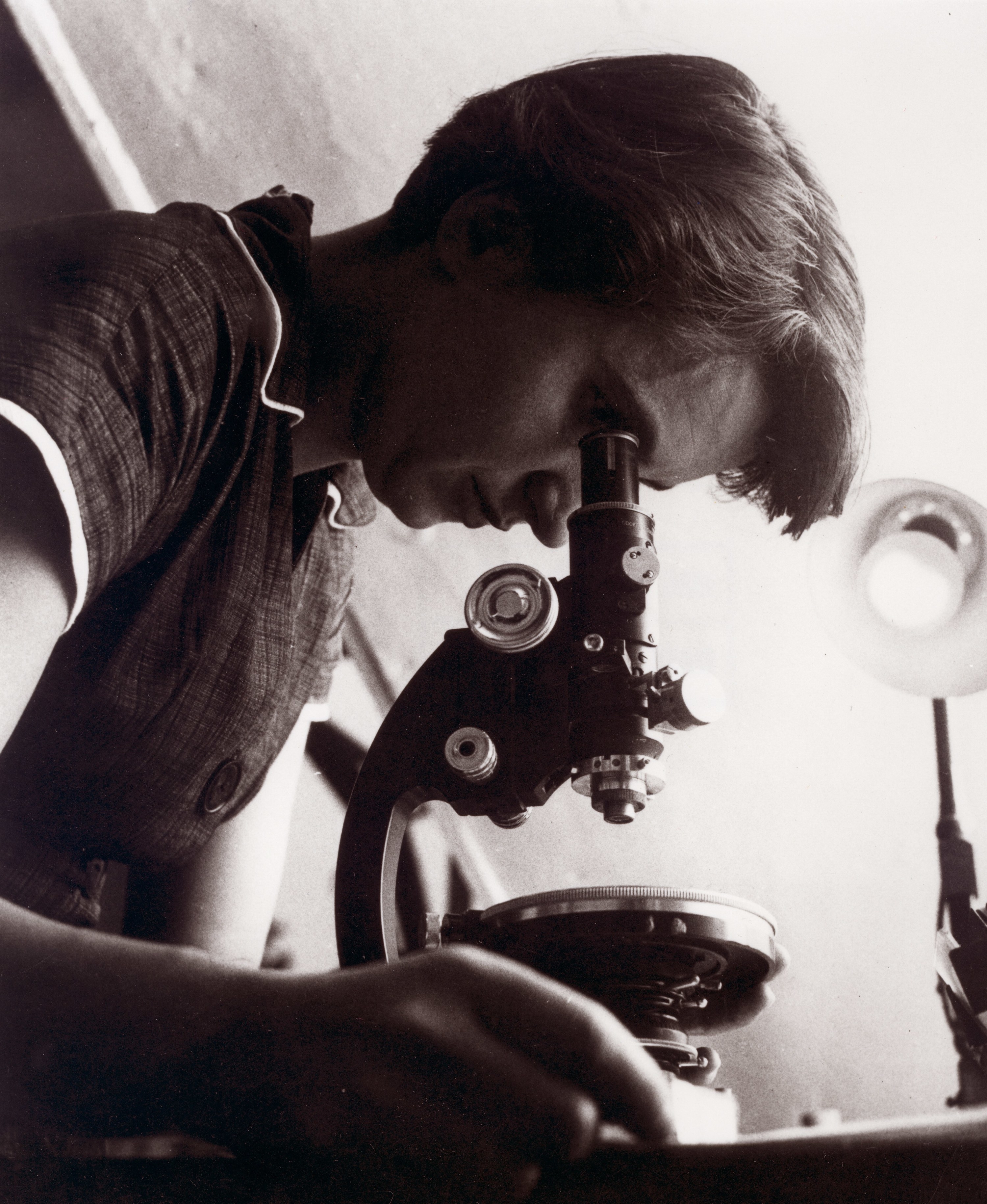 Rosalind looking down a microscope, wearing a tweed type dress.