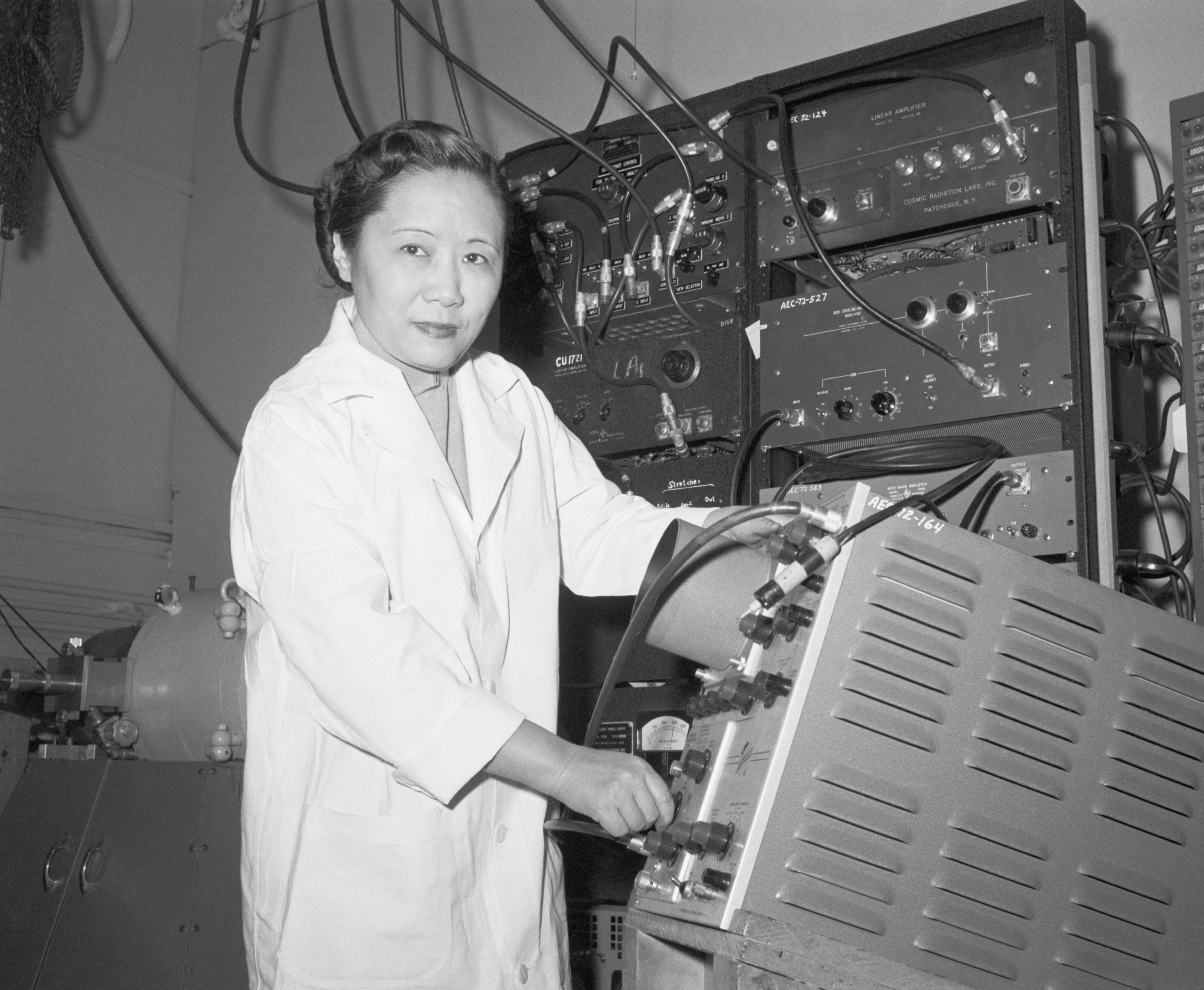 Dr Wu in a lab coat, using lab equipment and looking directly at the camera