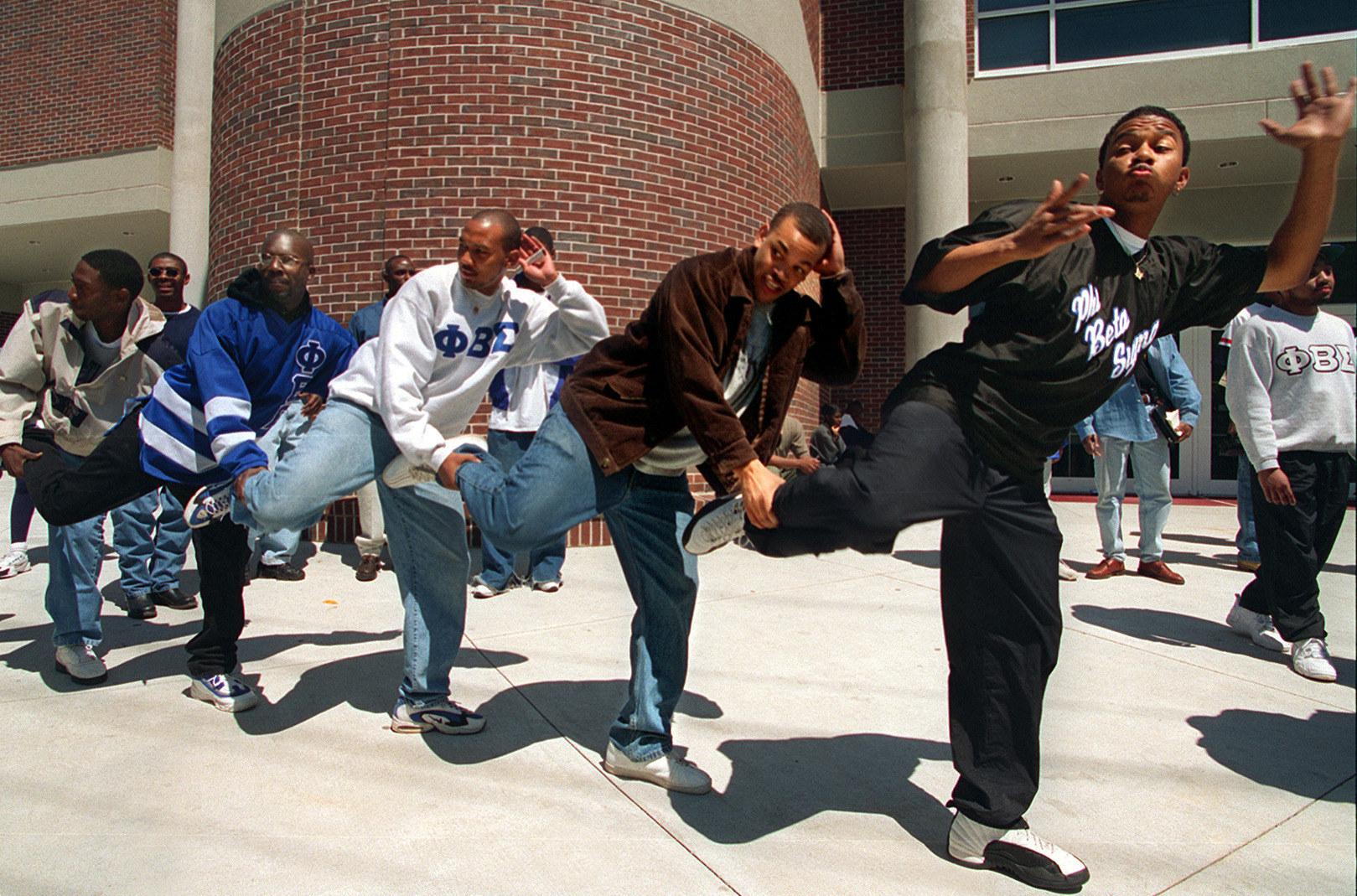 a line of men dance on campus in the sunshine 