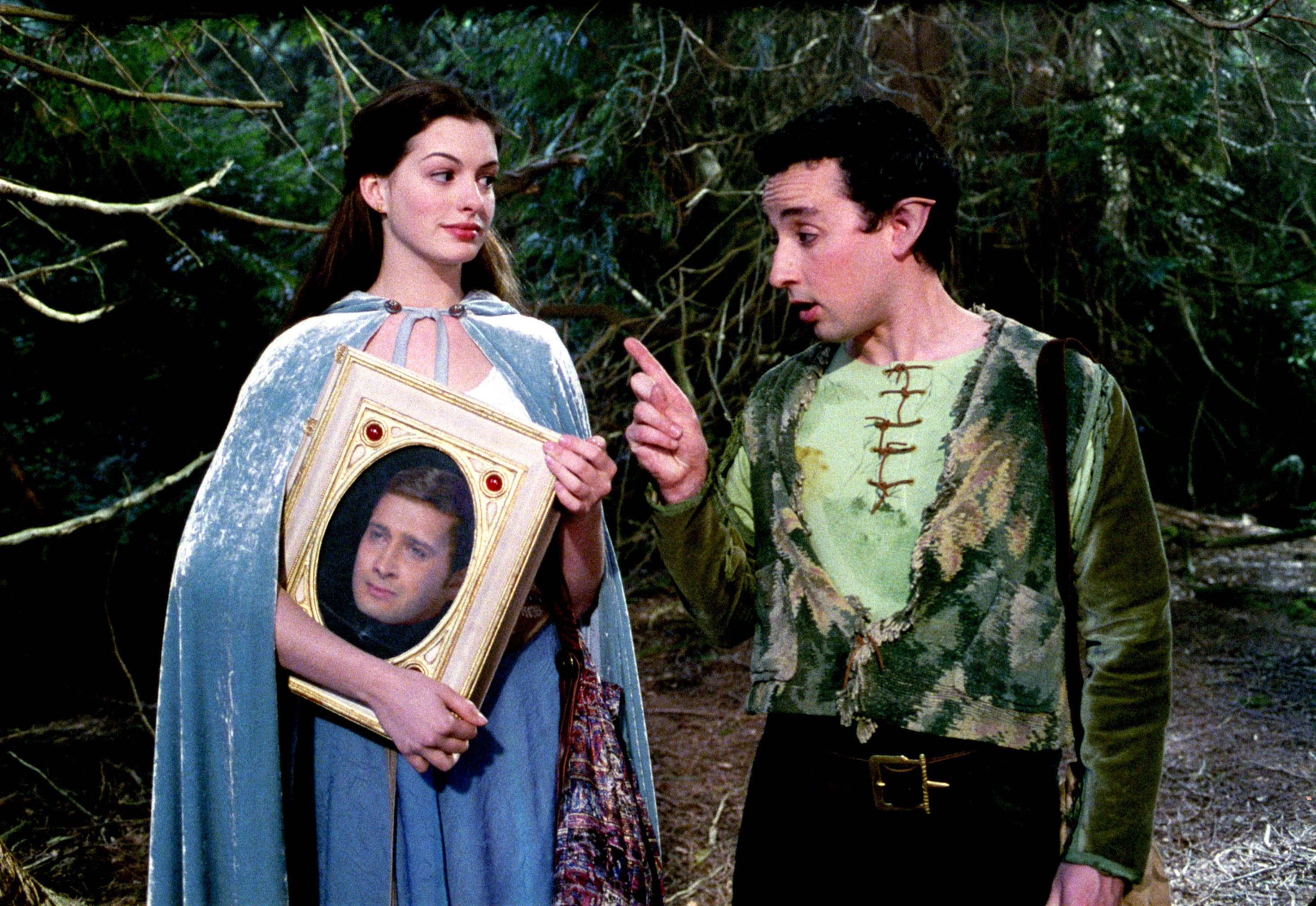 Anne Hathaway and Aidan McArdle standing in a forest in medieval clothing in ella enchanted