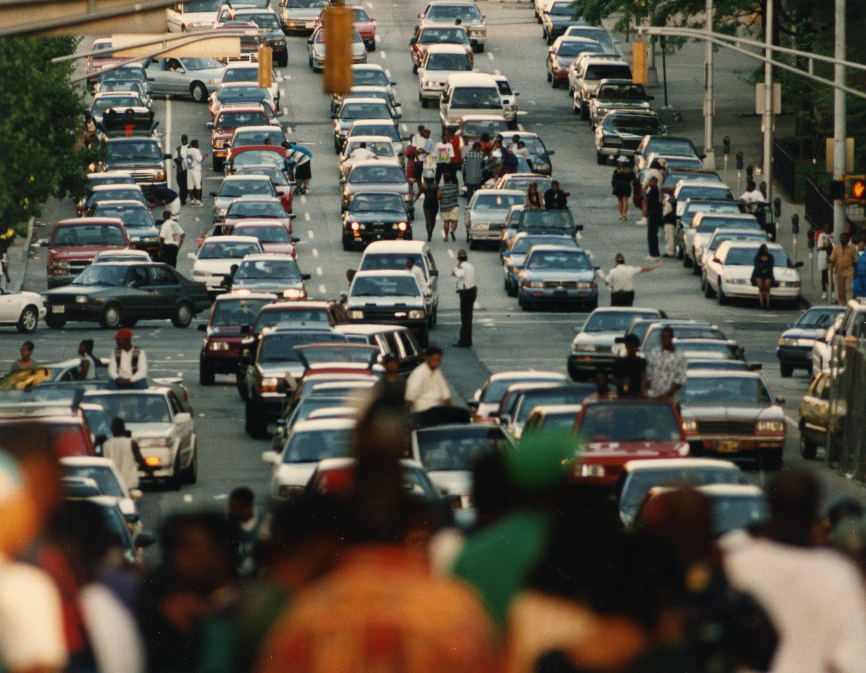 long lines of traffic with some people sitting on hoods of cars and others grouped on the street