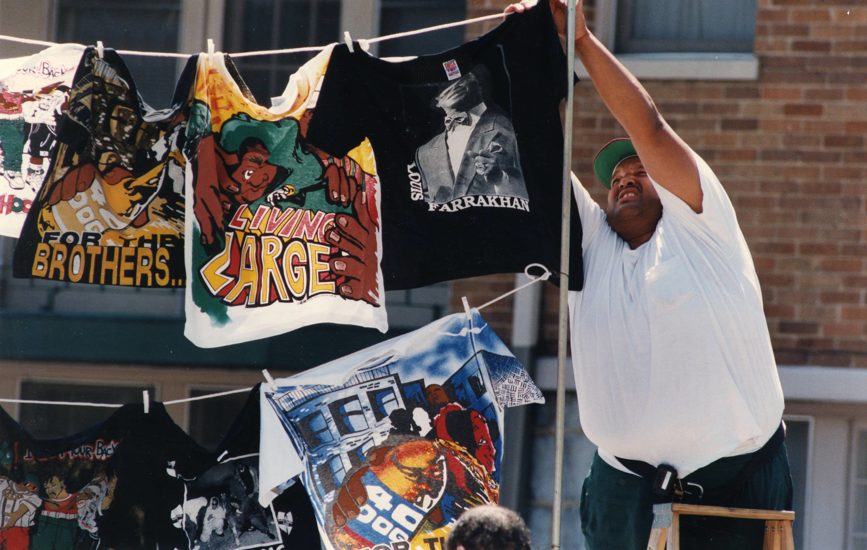a man hangs up t shirts for sale that read living large, for the brothers and louis farrakhan