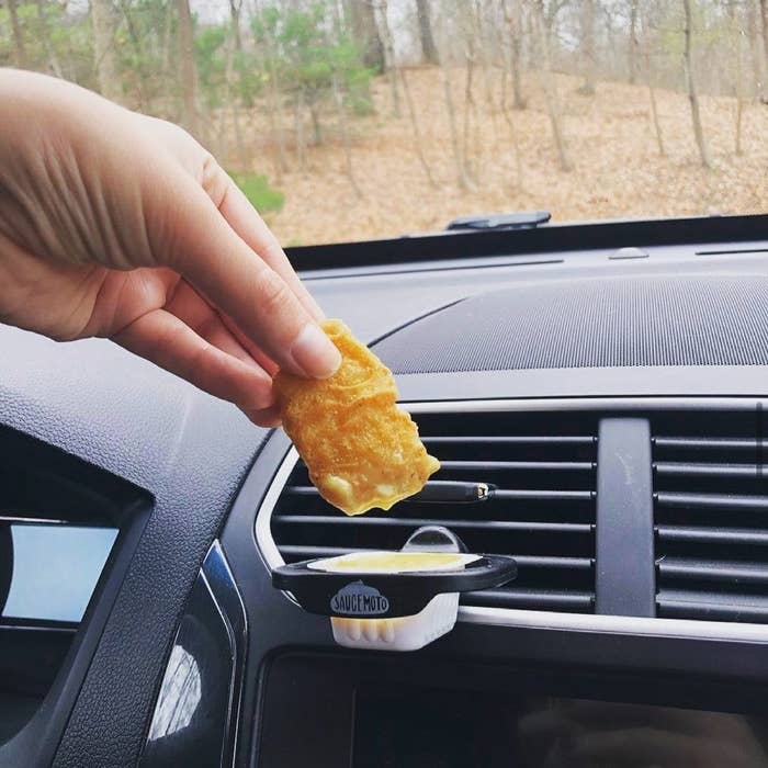 A person dunking a chicken nugget into a dip clip attached to a car vent