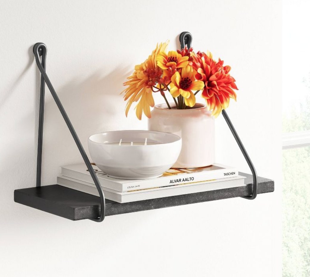 A black decorative wall shelf with books and flowers atop