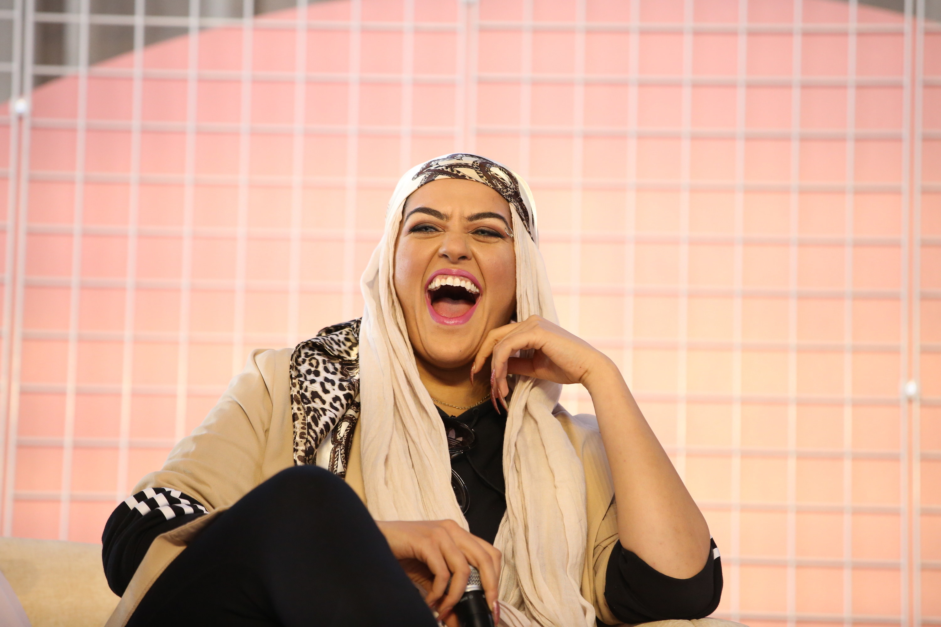 Amani Al-Khatahtbeh speaking at Girlboss Rally NYC 2018. She is laughing in front of a pink background.