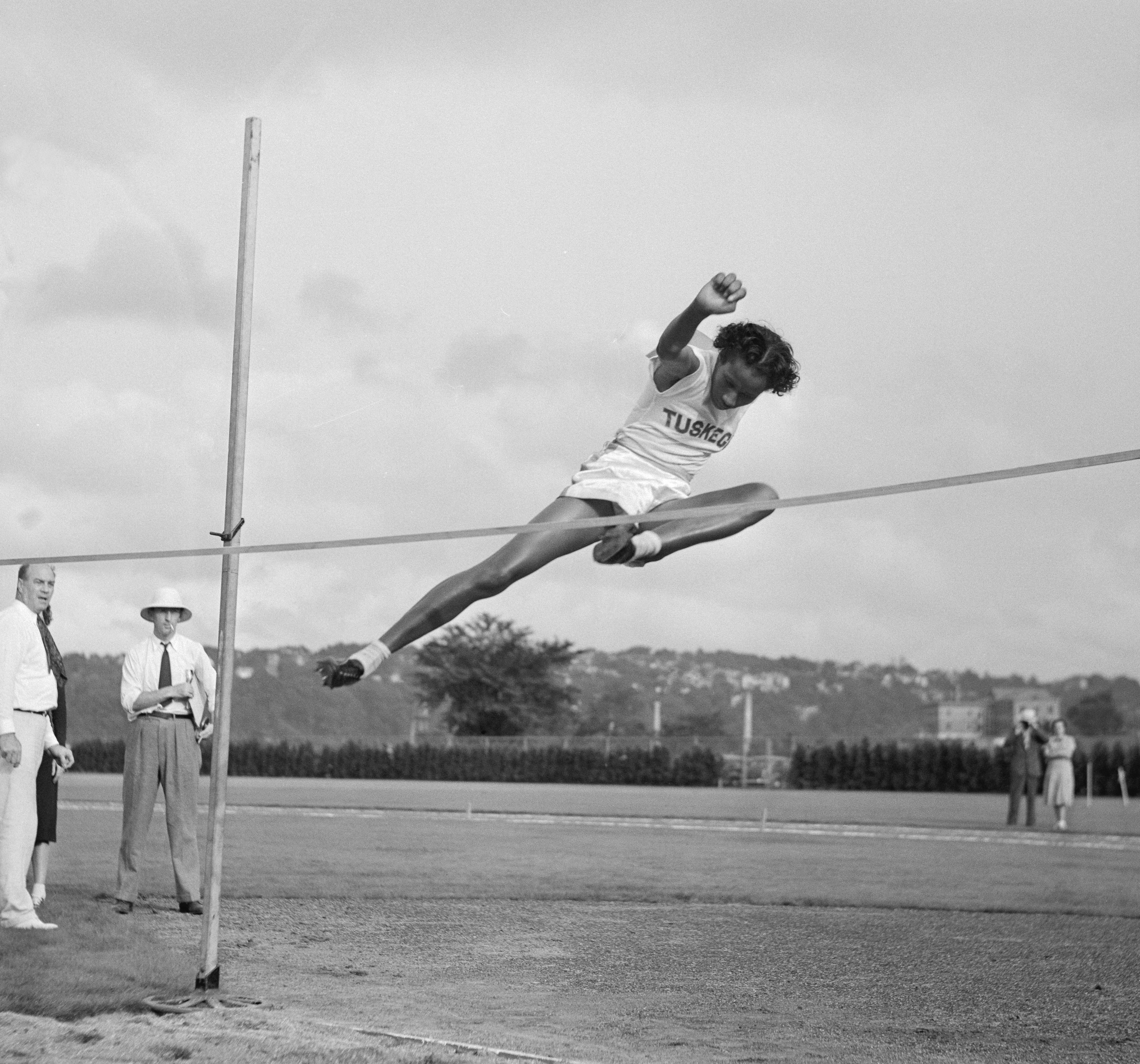 Alice Coachman leaping over a high jump bar outdoors at the National Women&#x27;s Track and Field meet