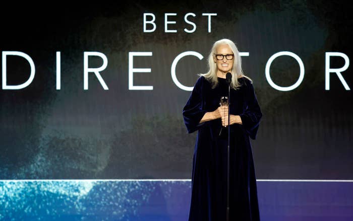 Jane clutches her award in front of a display that says "Best Director"