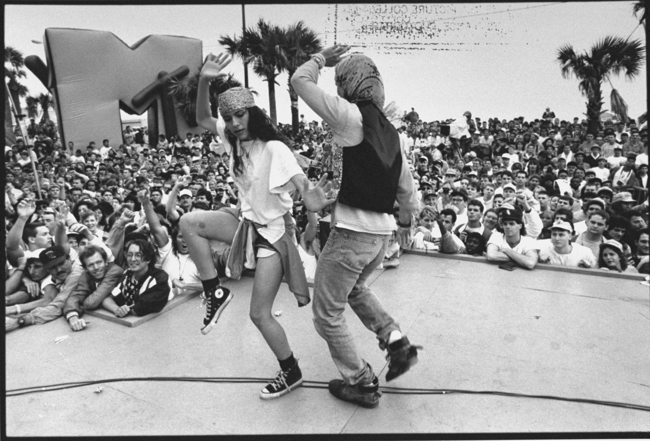 two people dance on stage in front of a huge crowd with a large inflatable MTV logo behind them 