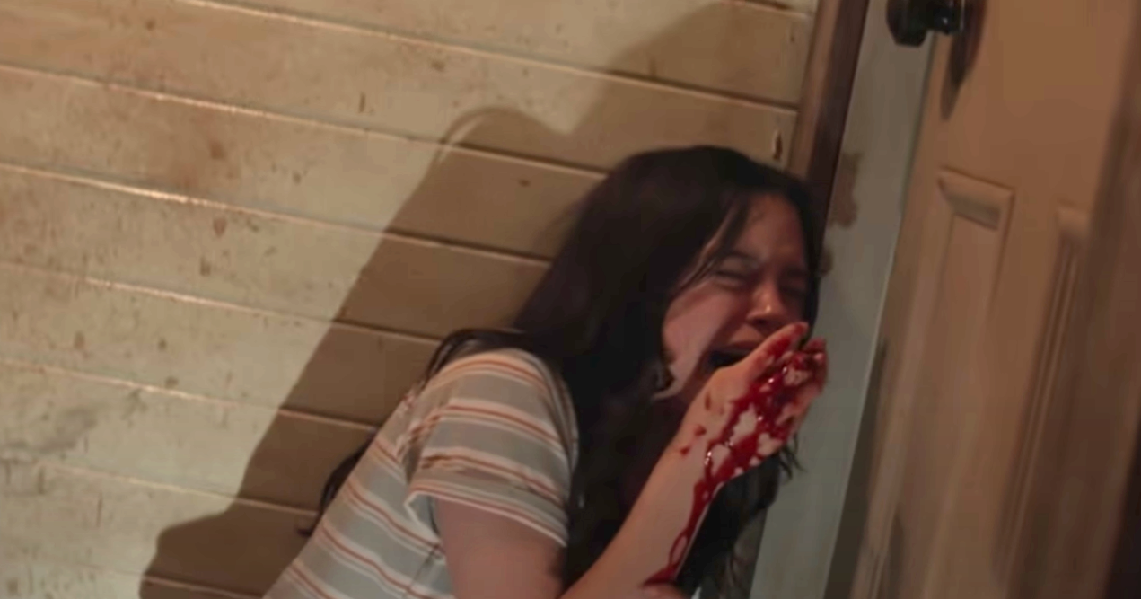 A woman screaming, covering her mouth, hand covered in blood