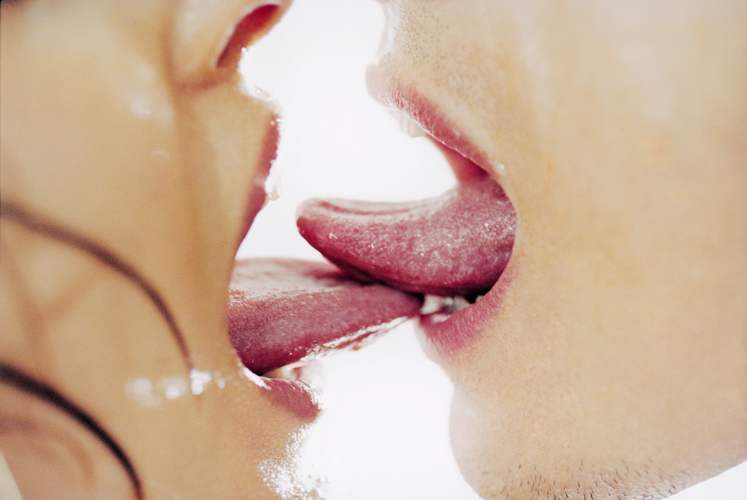 A close-up image of two people swapping saliva and touching tongues