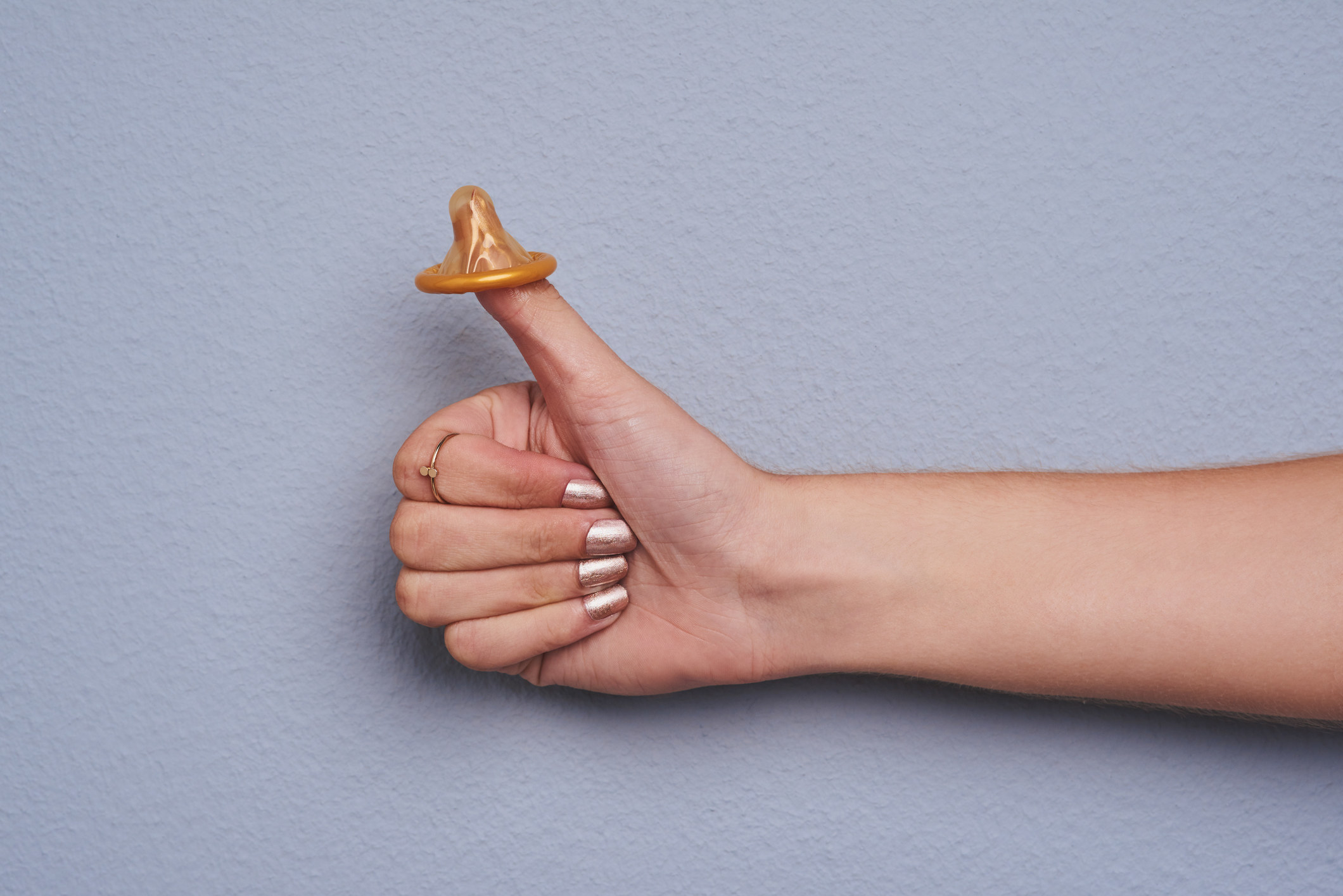 a person&#x27;s hand in a thumbs-up position with the top of a condom on the thumb
