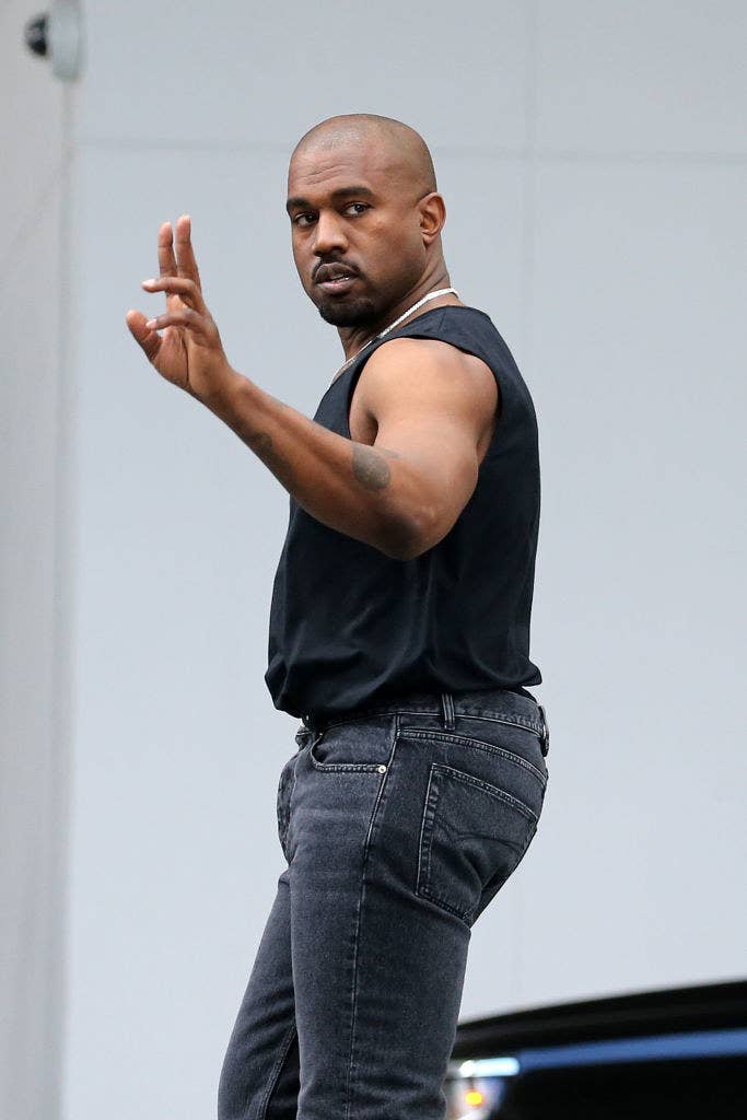 Kanye wearing jeans and a sleeveless T-shirt holds up the peace sign