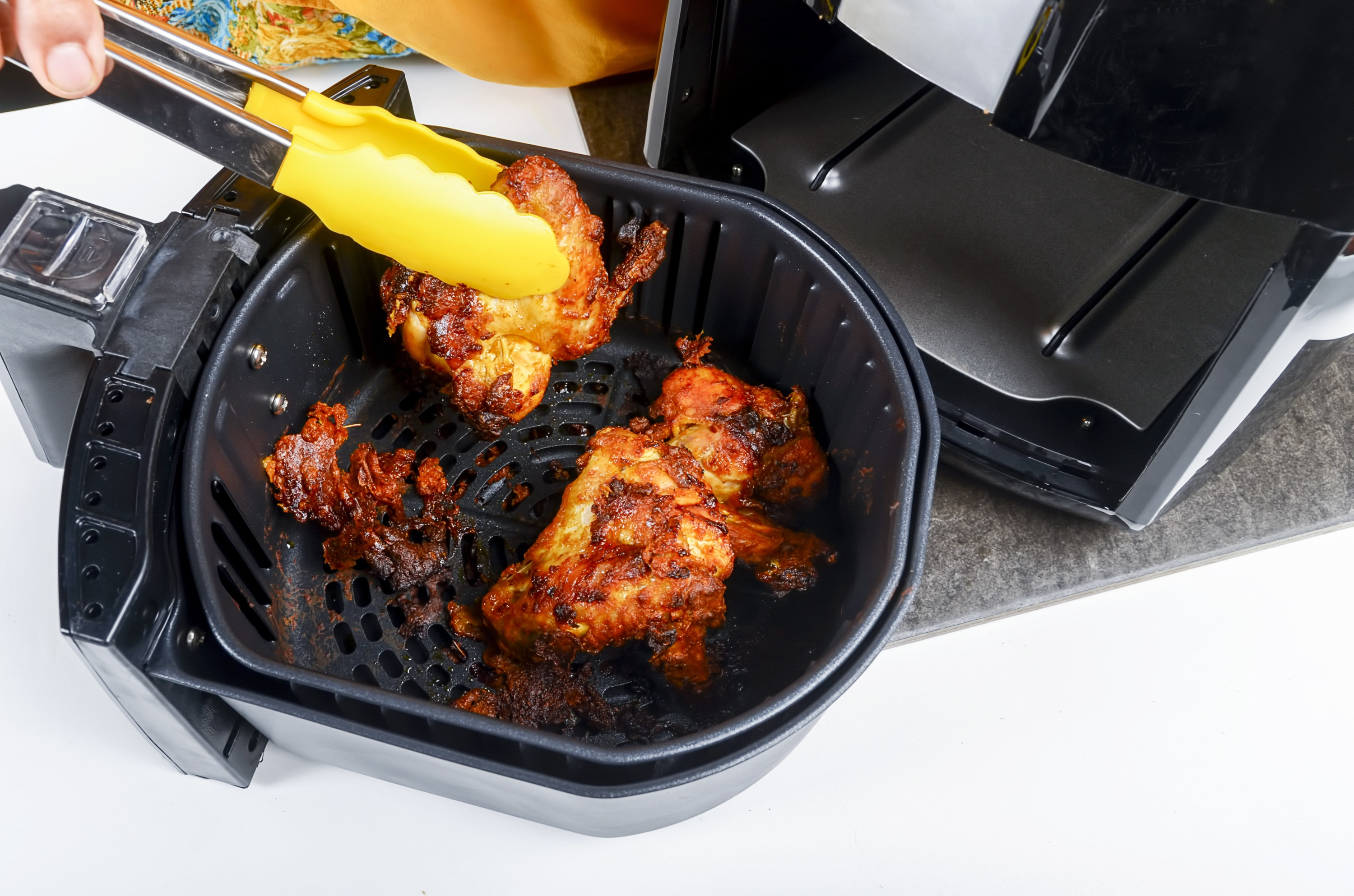 Removing sticky saucy meat from air fryer basket with tongs