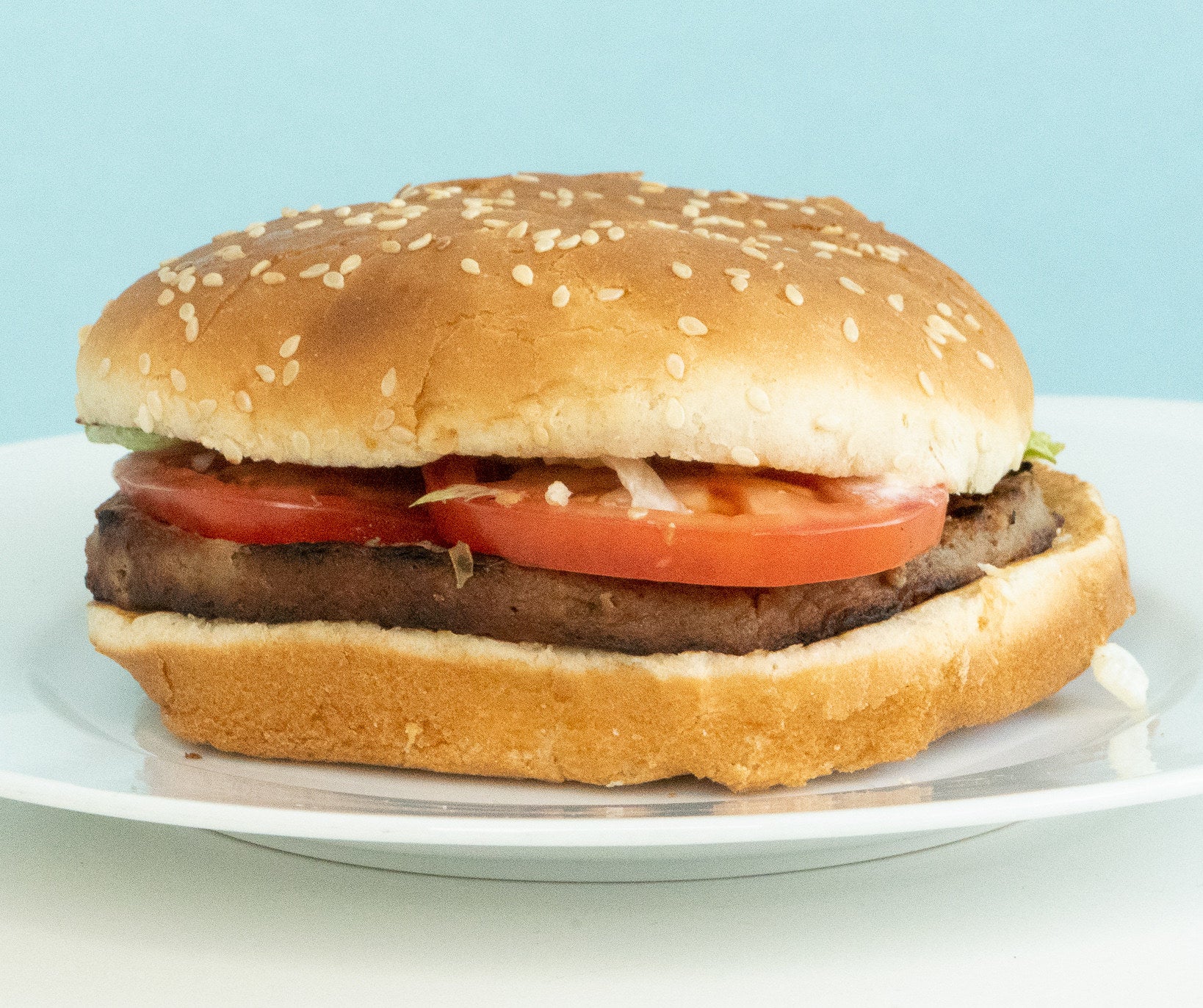 a flat burger with tomatoes exposed and a sesame seed bun