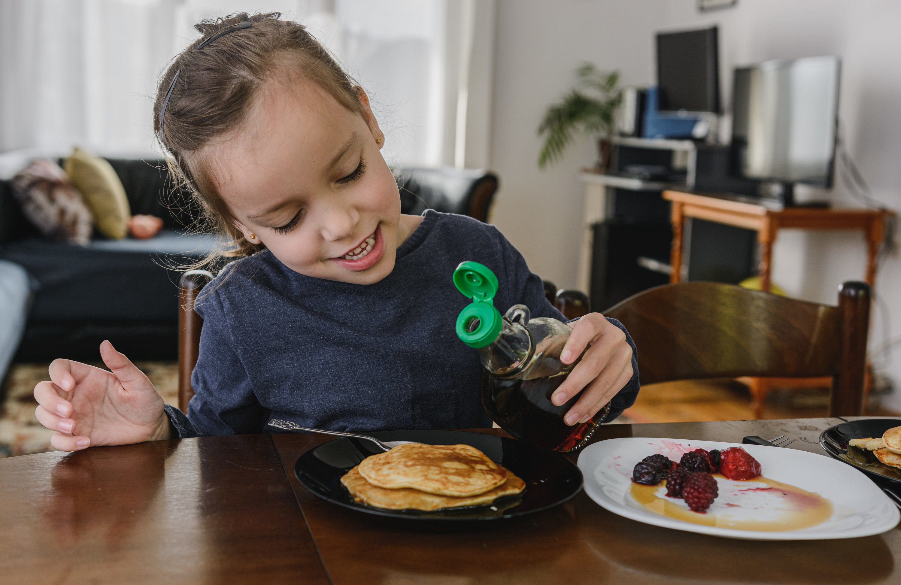 Child drizzling syrup over pancakes on a plate
